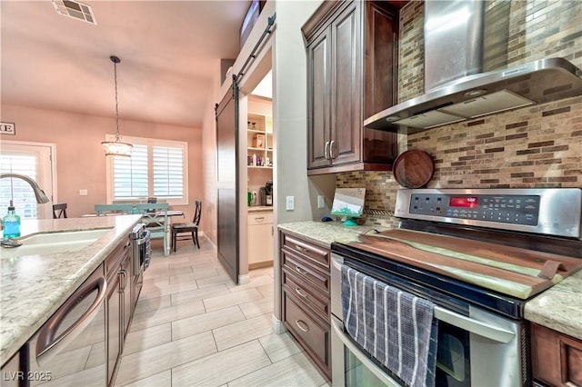 kitchen with sink, a barn door, stainless steel appliances, light stone countertops, and wall chimney exhaust hood