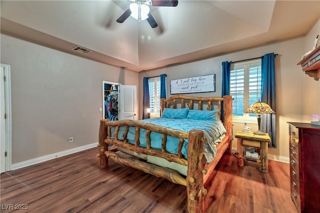 bedroom featuring hardwood / wood-style flooring, a raised ceiling, a walk in closet, and ceiling fan