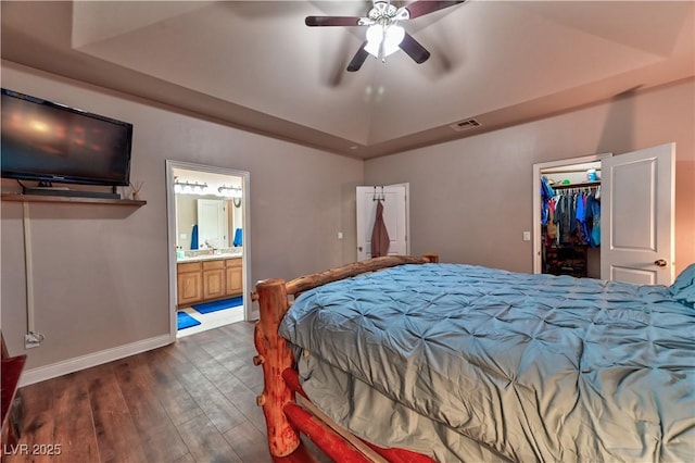 bedroom with a tray ceiling, a walk in closet, ensuite bath, and dark hardwood / wood-style floors