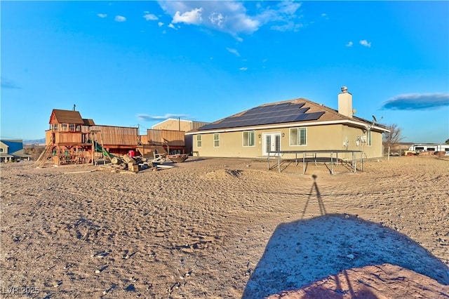 back of house featuring a playground and solar panels