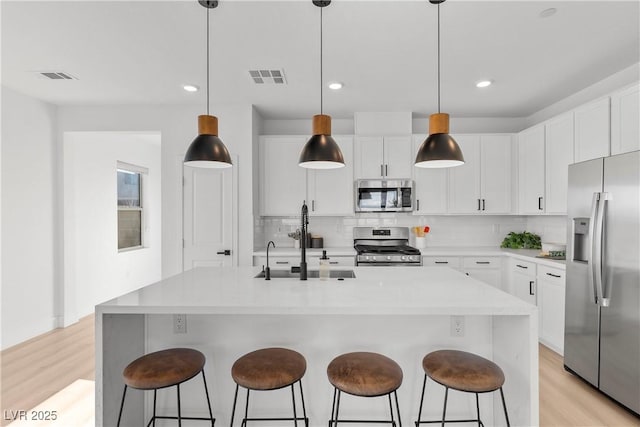 kitchen with stainless steel appliances, white cabinetry, and a kitchen island with sink