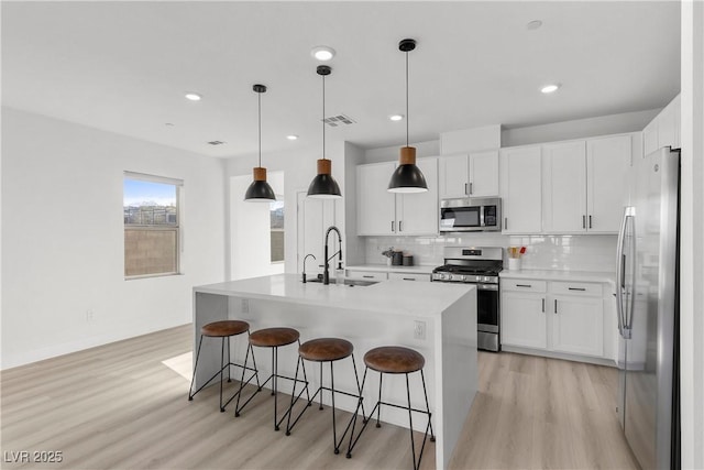 kitchen with stainless steel appliances, a kitchen island with sink, sink, and white cabinets