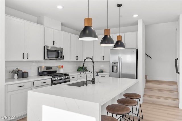 kitchen featuring stainless steel appliances, sink, white cabinets, and a kitchen island with sink