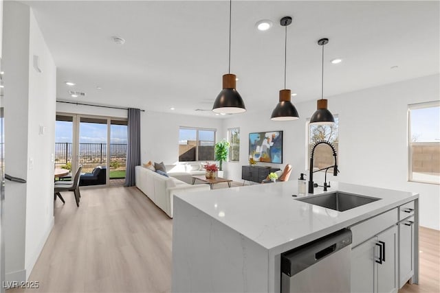 kitchen with sink, dishwasher, light stone counters, an island with sink, and decorative light fixtures