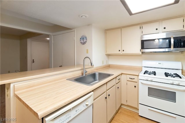 kitchen with sink, white appliances, light hardwood / wood-style floors, kitchen peninsula, and cream cabinetry