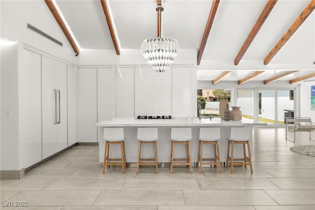 kitchen featuring pendant lighting, a breakfast bar area, an inviting chandelier, beam ceiling, and white cabinets