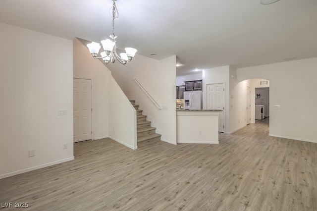 unfurnished living room with an inviting chandelier, light wood-type flooring, baseboards, and arched walkways