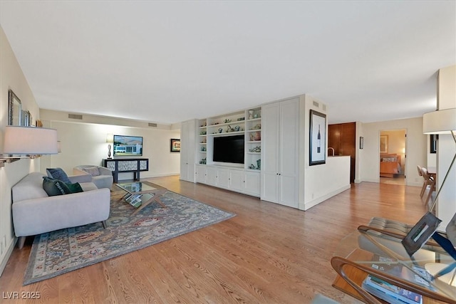 living room featuring built in shelves, light wood-type flooring, visible vents, and baseboards