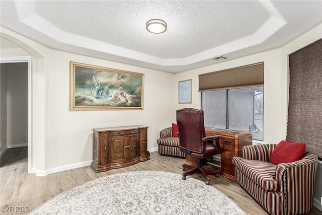 living area featuring a textured ceiling, light hardwood / wood-style flooring, and a raised ceiling