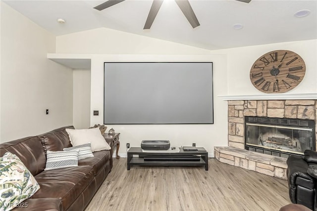 living room with ceiling fan, lofted ceiling, a stone fireplace, and light hardwood / wood-style flooring