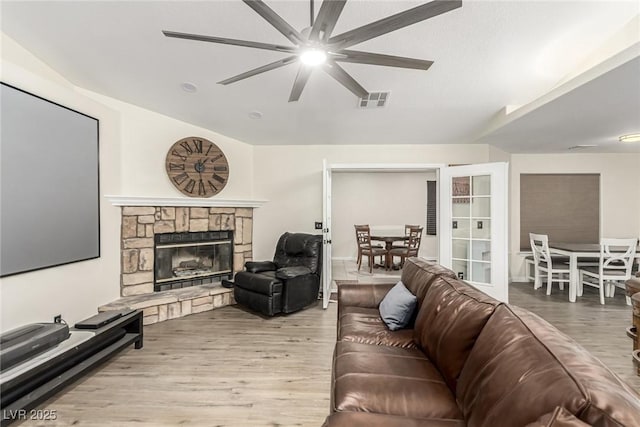 living room with light hardwood / wood-style floors, lofted ceiling, ceiling fan, and a fireplace