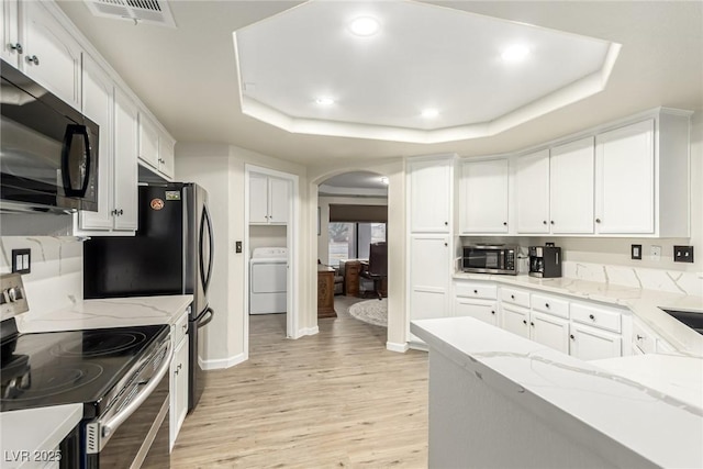 kitchen featuring light wood-type flooring, a tray ceiling, stainless steel appliances, washer / clothes dryer, and white cabinets