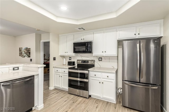 kitchen featuring white cabinets, light wood-type flooring, stainless steel appliances, and a raised ceiling