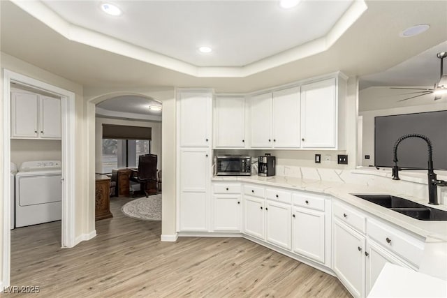 kitchen featuring light hardwood / wood-style floors, a tray ceiling, sink, washer and dryer, and white cabinetry