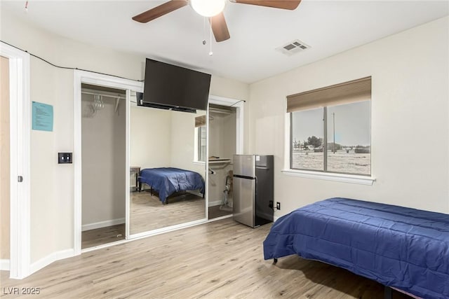 bedroom featuring stainless steel refrigerator, light wood-type flooring, ceiling fan, and multiple windows