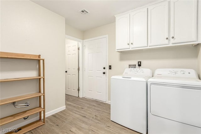 clothes washing area with washing machine and clothes dryer, light hardwood / wood-style floors, and cabinets