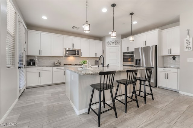 kitchen featuring white cabinetry, pendant lighting, stainless steel appliances, and an island with sink