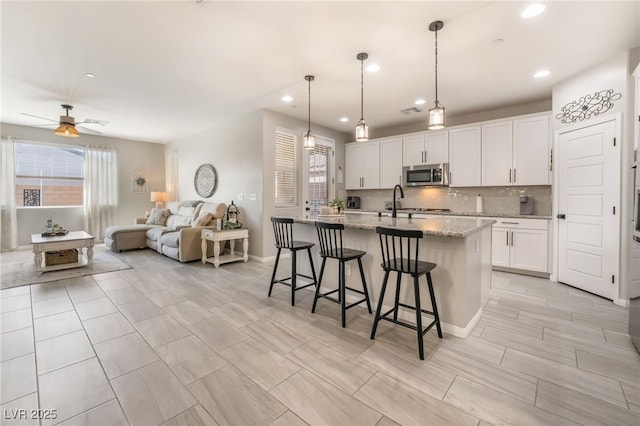 kitchen with a breakfast bar, white cabinetry, an island with sink, pendant lighting, and light stone countertops