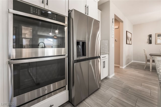 kitchen with white cabinetry, appliances with stainless steel finishes, and light stone counters