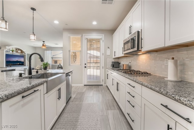 kitchen featuring hanging light fixtures, stainless steel appliances, white cabinets, and light stone countertops