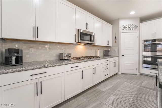 kitchen featuring light stone countertops, appliances with stainless steel finishes, white cabinets, and decorative backsplash