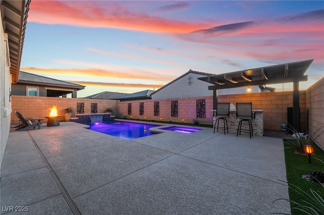 pool at dusk with pool water feature, a patio, exterior bar, and an in ground hot tub