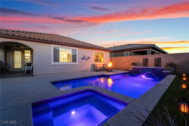 pool at dusk featuring an in ground hot tub and a patio