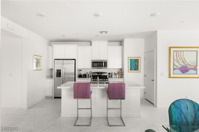 kitchen with a center island with sink, a breakfast bar, white cabinets, and appliances with stainless steel finishes