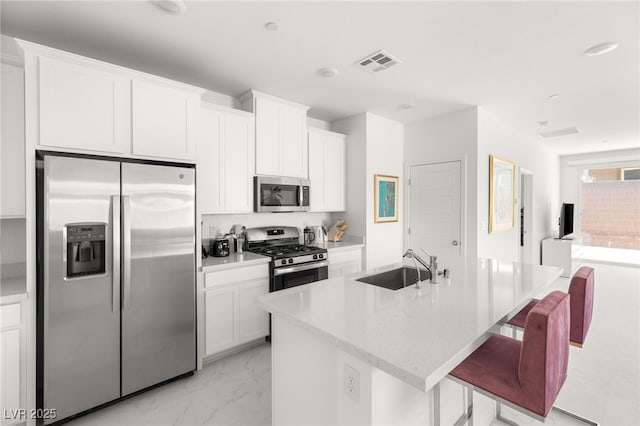 kitchen with appliances with stainless steel finishes, white cabinetry, sink, a breakfast bar area, and a kitchen island with sink