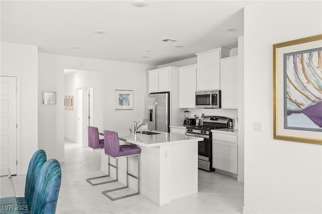 kitchen with appliances with stainless steel finishes, sink, a kitchen island with sink, and white cabinets