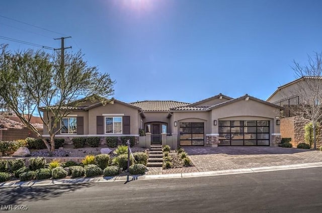 mediterranean / spanish home with a garage, a tiled roof, decorative driveway, and stucco siding