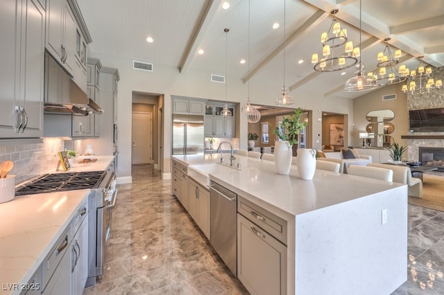 kitchen featuring decorative light fixtures, stainless steel appliances, visible vents, a sink, and a large island with sink