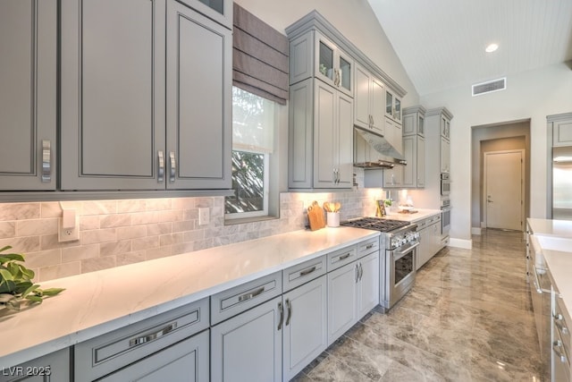 kitchen with high end stove, under cabinet range hood, visible vents, vaulted ceiling, and glass insert cabinets