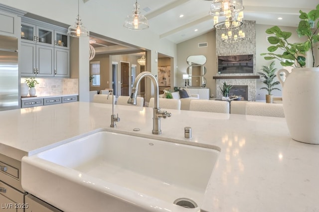 room details featuring hanging light fixtures, glass insert cabinets, a large fireplace, a sink, and beamed ceiling