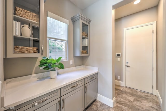 interior space with baseboards, light countertops, glass insert cabinets, and gray cabinetry