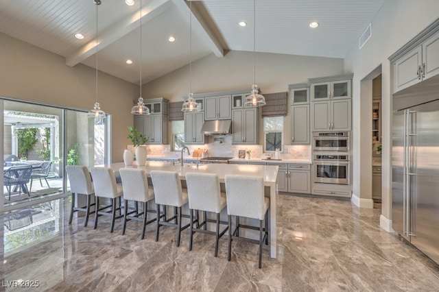 kitchen featuring decorative light fixtures, light countertops, appliances with stainless steel finishes, glass insert cabinets, and under cabinet range hood