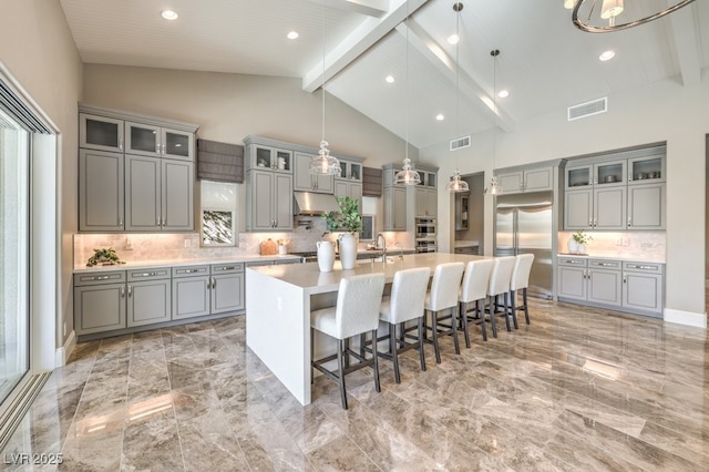 kitchen with visible vents, glass insert cabinets, decorative light fixtures, light countertops, and a large island with sink