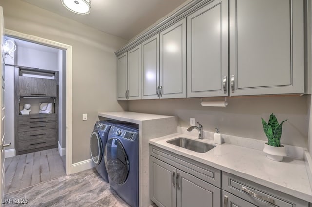 laundry area with cabinet space, baseboards, light wood-style flooring, independent washer and dryer, and a sink