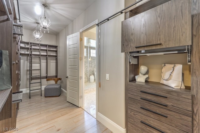 walk in closet featuring light wood finished floors, a barn door, and a chandelier