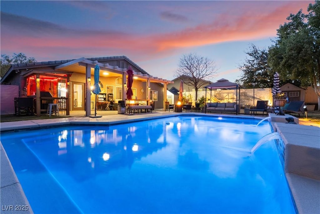 pool at dusk with an outdoor living space, pool water feature, and a patio area