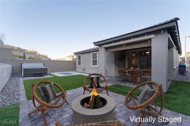 back house at dusk with a patio, a hot tub, and a fire pit