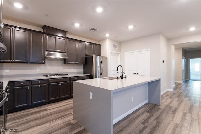 kitchen with appliances with stainless steel finishes, a kitchen island with sink, sink, and light hardwood / wood-style flooring