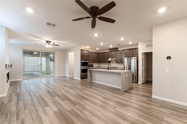 kitchen featuring sink, light hardwood / wood-style flooring, dark brown cabinets, stainless steel appliances, and an island with sink