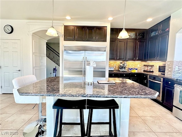 kitchen with pendant lighting, stainless steel appliances, dark stone counters, and a kitchen island