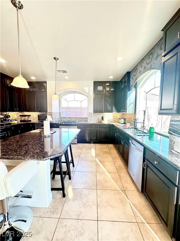 kitchen with pendant lighting, dark stone countertops, backsplash, a kitchen breakfast bar, and stainless steel dishwasher