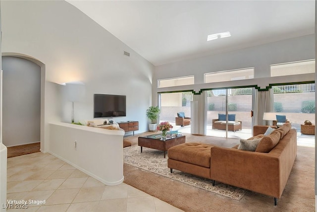 living area featuring light tile patterned floors, high vaulted ceiling, arched walkways, visible vents, and baseboards