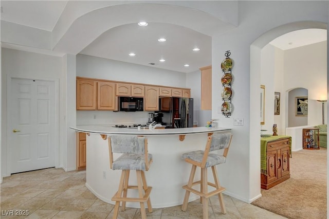 kitchen with light countertops, light brown cabinetry, black appliances, a peninsula, and a kitchen bar