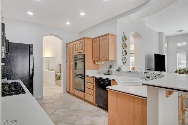 kitchen with arched walkways, black appliances, light brown cabinetry, and light countertops