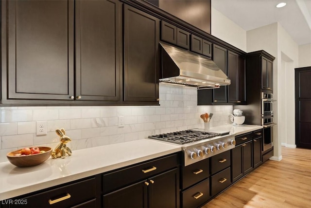 kitchen with dark brown cabinetry, appliances with stainless steel finishes, decorative backsplash, and light wood-type flooring