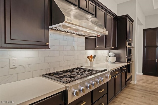 kitchen featuring extractor fan, backsplash, stainless steel gas cooktop, dark brown cabinetry, and light wood-type flooring